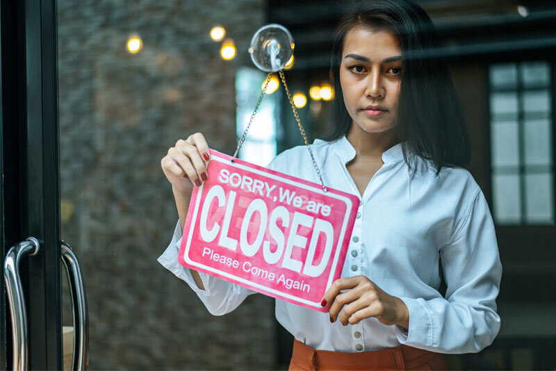 Women in Storefront Holding Close Sign